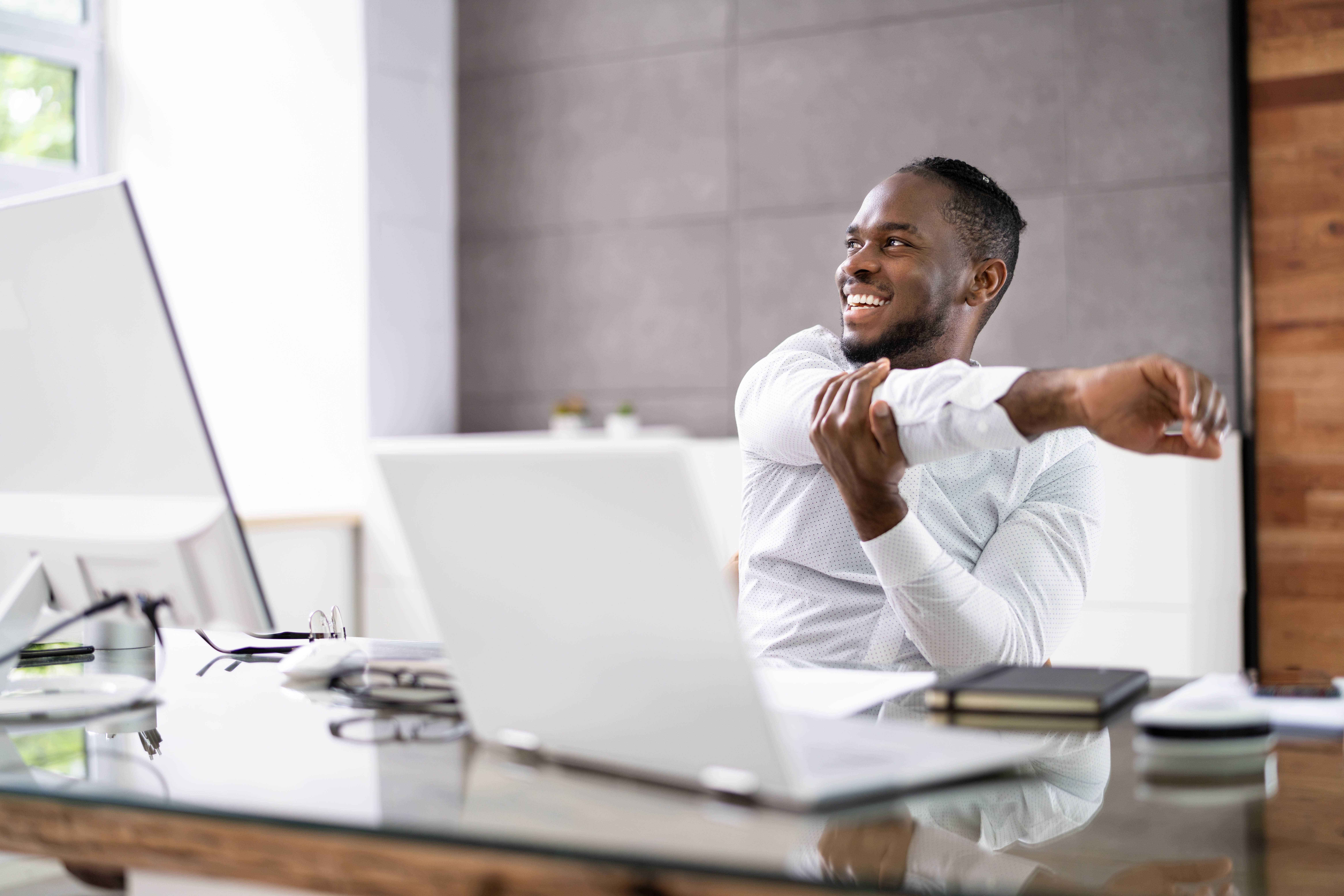 Young black man stretching his arms while he sits at his desk, looking out the window Young black man stretching his arms while he sits at his desk, looking out the window